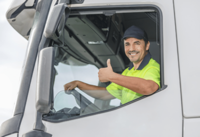 an hgv driver in high-vis is sitting in a white vehicle and making a thumbs up sign.